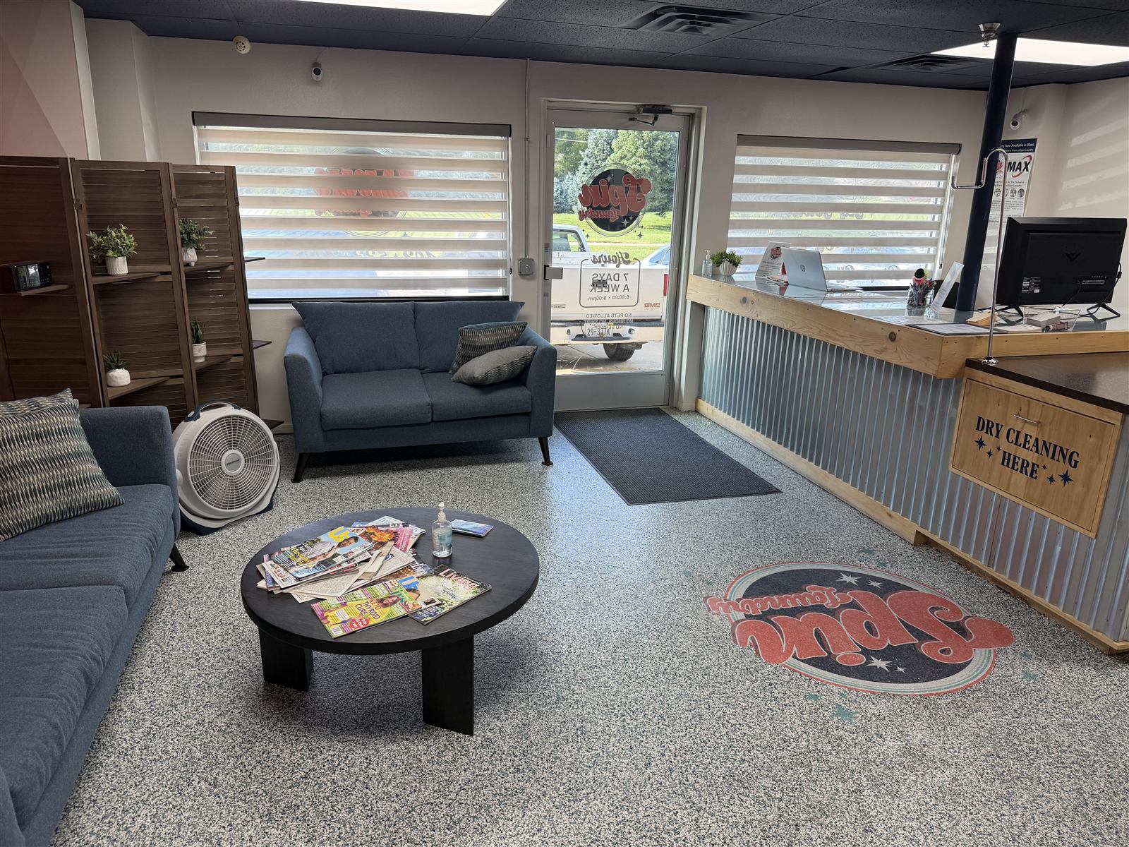 The Spin Laundry lounge with blue sofas, a round coffee table with magazines, and the Spin Laundry logo on the floor