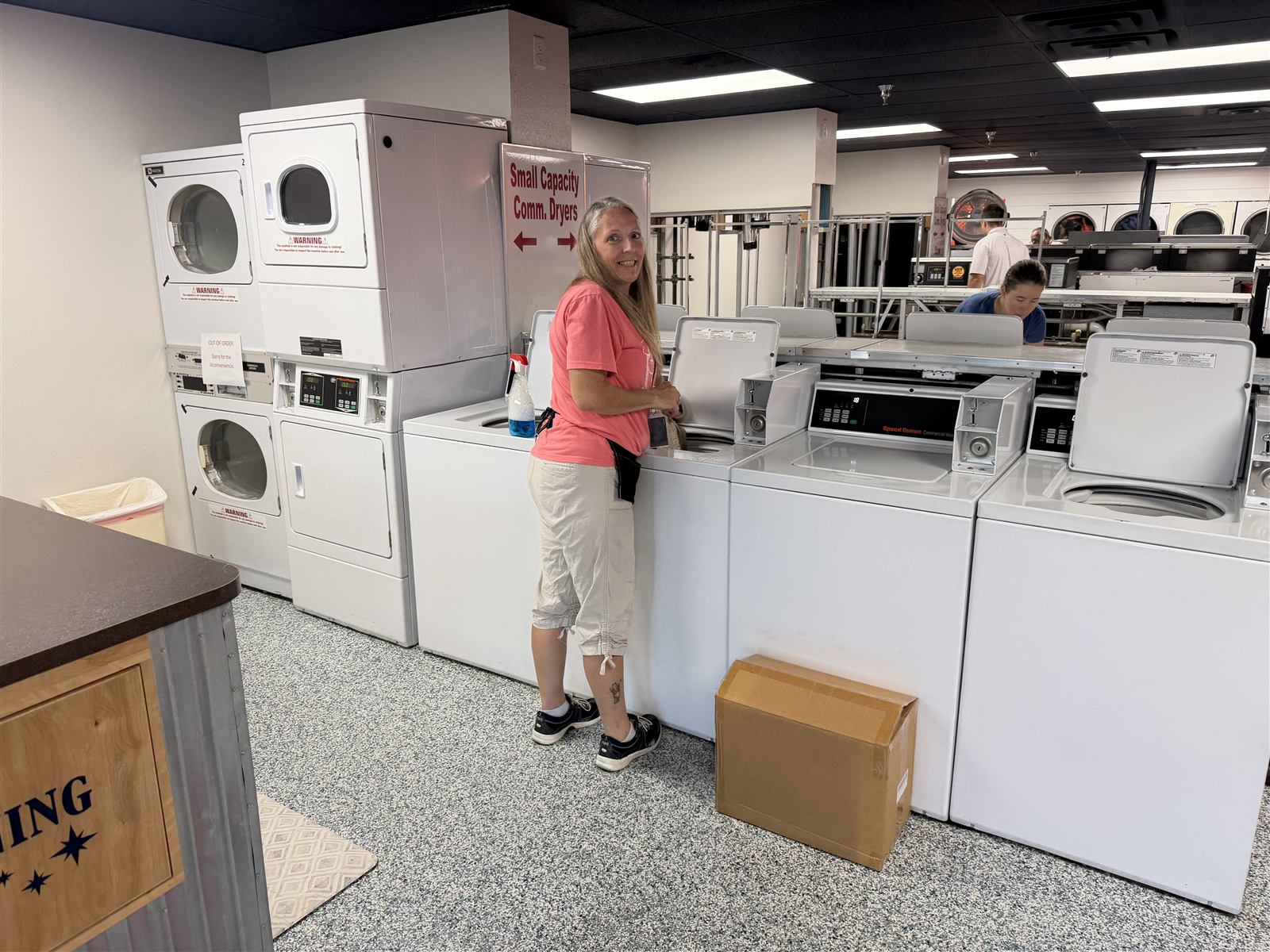 A Spin Laundry team member smiling beside a row of top-load washers